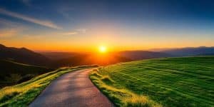 A winding path leads to mountains under a sunrise.