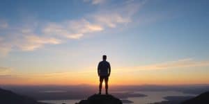 Person gazing at calm lake, mountains, sunrise.