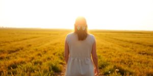Person walking through a sunlit field, looking forward.