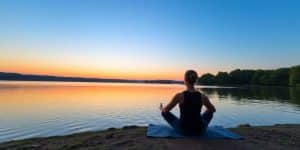 Person meditating by a peaceful lake at sunrise.
